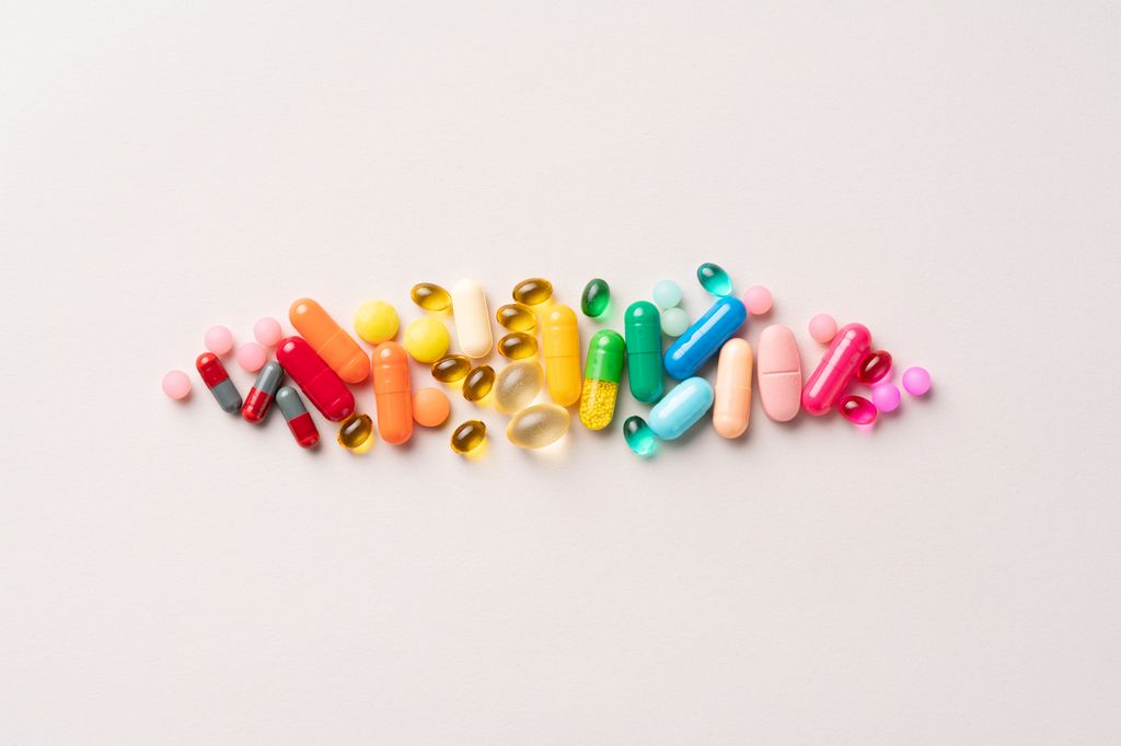 A Group of Multi Colored Medical Pills Organized in a Row Directly Above View on Beige Background.