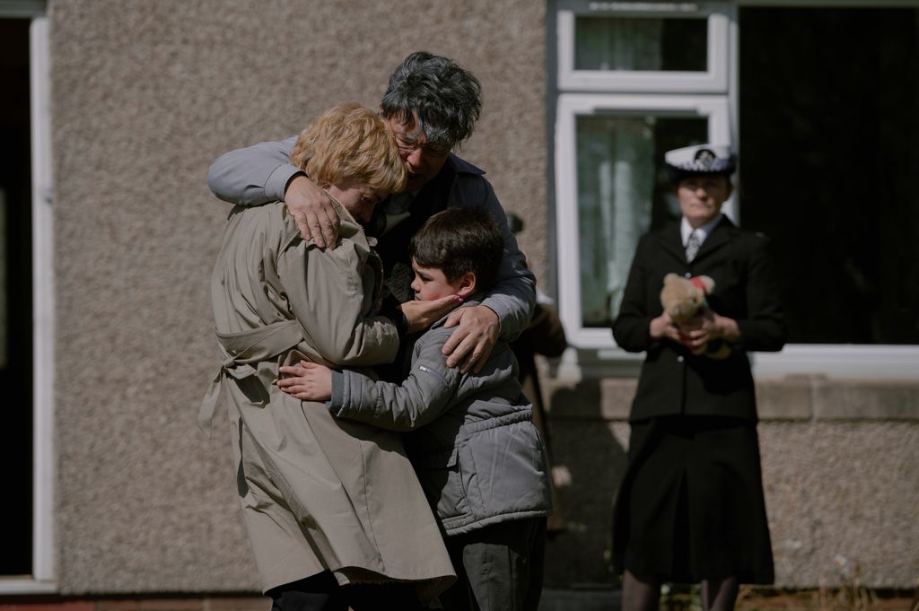 A family hug outside of a house next to police