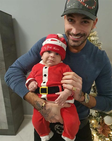 Giovanni Pernice holding a baby in a Santa suit
