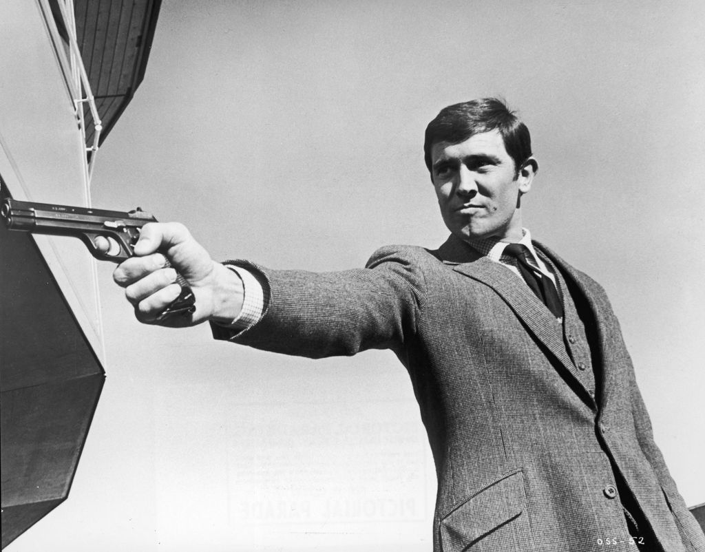 Promotional portrait of Australian actor George Lazenby aiming a gun for the James Bond film, 'On Her Majesty's Secret Service,' directed by Peter Hunt, 1969.