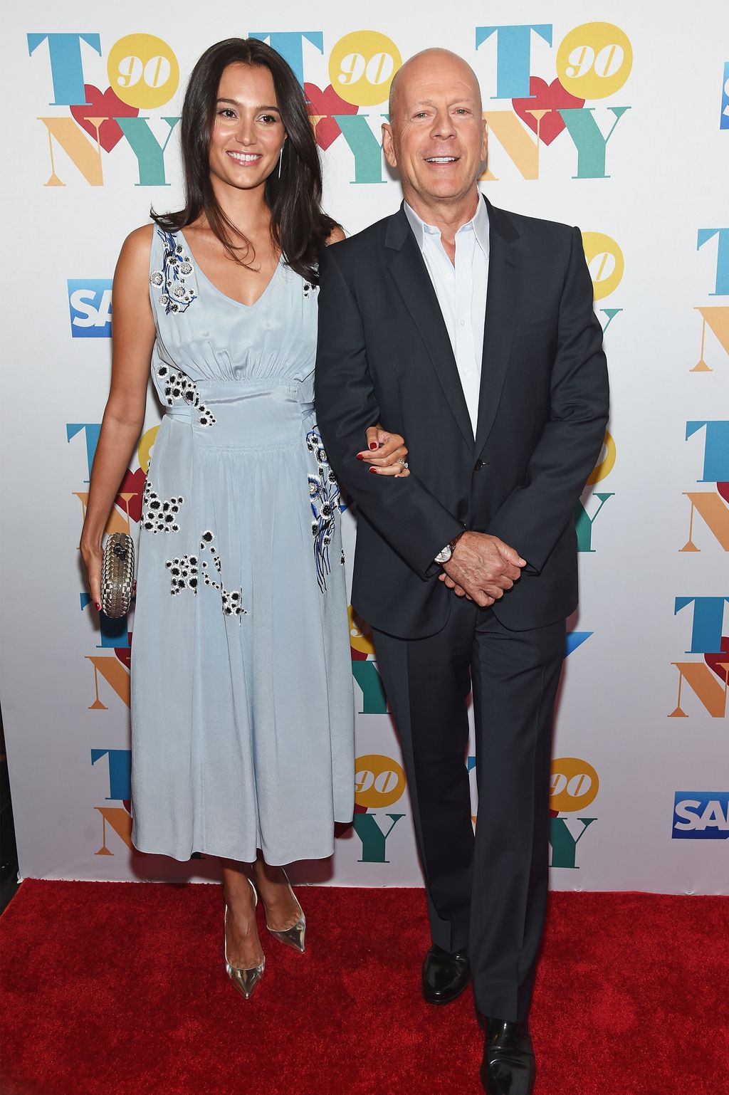 Emma Heming Willis and Bruce Willis smiling which being photo'd at a red carpet event 