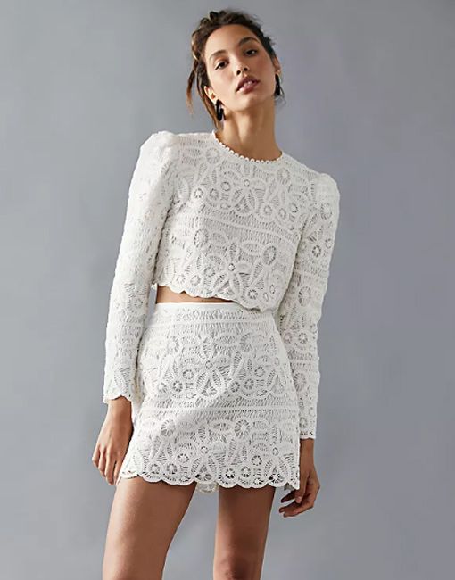 model wears a long sleeved white lace crop top and matching mini skirt