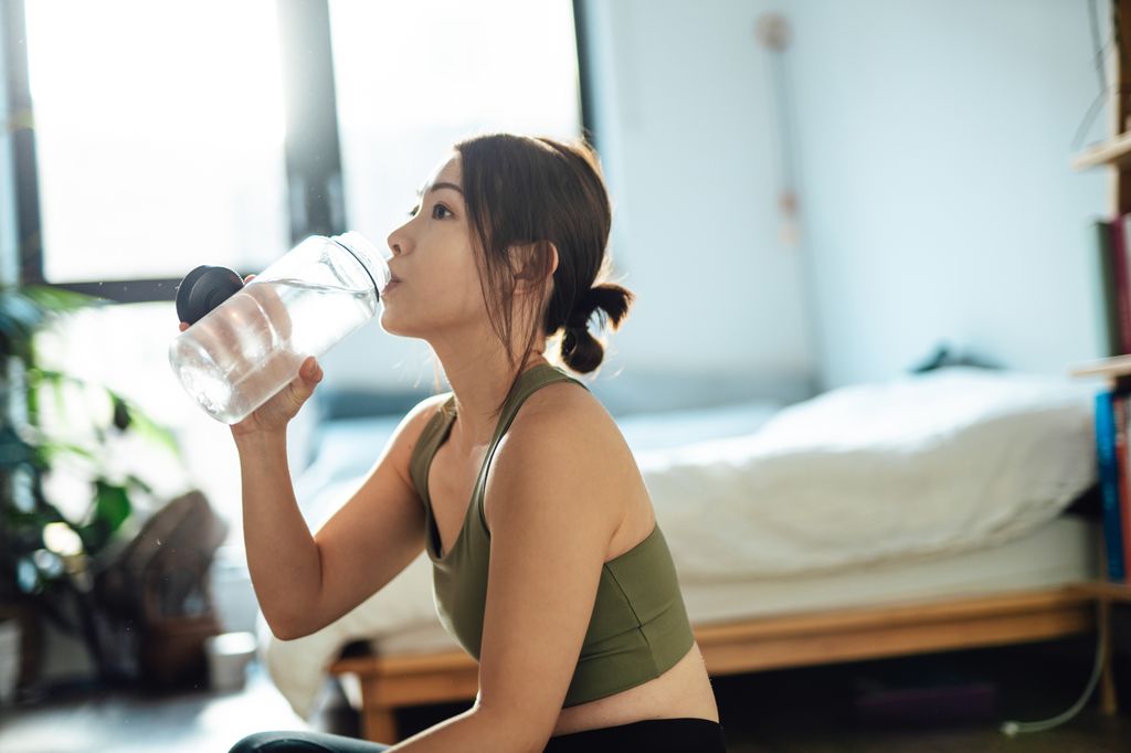 Young Asian woman drinking water after exercising at home