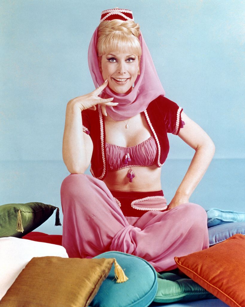 Barbara Eden wearing a pink set, sat on the floor surrounded by cushions