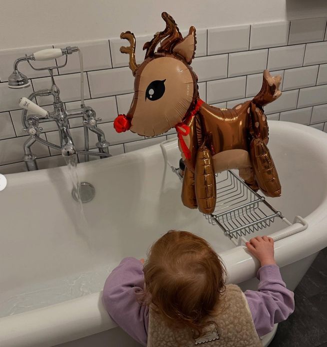 a young girl by a bathtub with a reindeer balloon