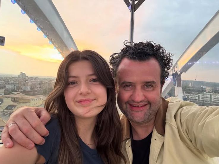 Daniel Mays with his arm around his daughter while they ride a Ferris wheel