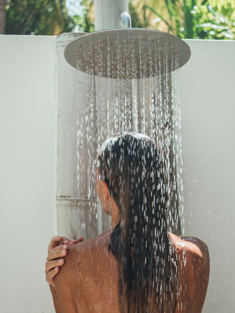 Woman takes outdoor shower in tropical garden