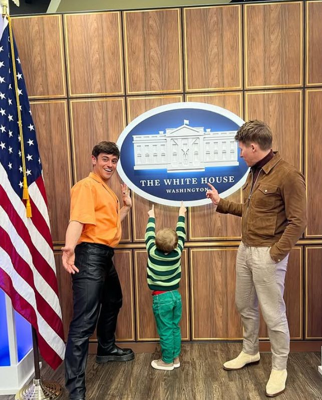 Tom Daley, Dustin Lance Black and their son outside a sign of The White House