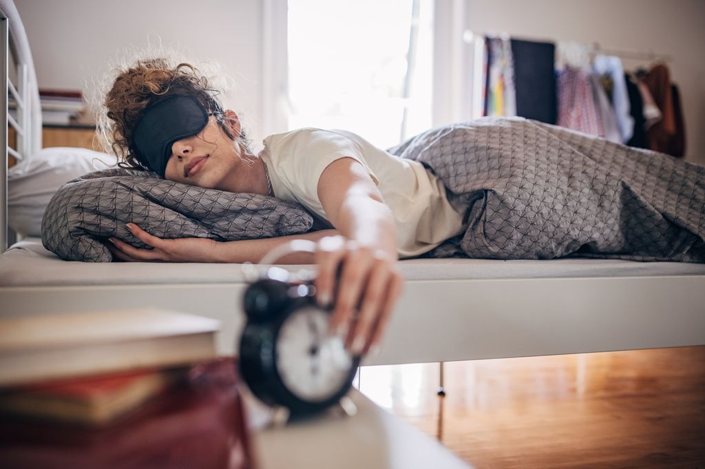 Femme au lit avec masque de sommeil en tenant le réveil qui s'éteint