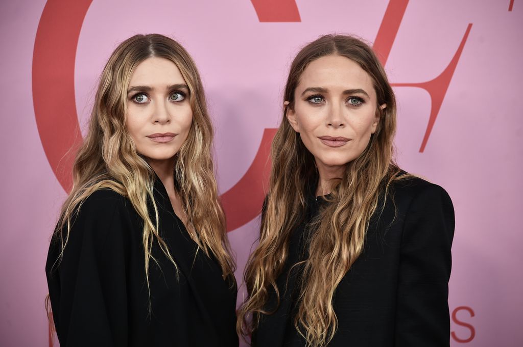 Ashley Olsen and Mary-Kate Olsen with long blonde hair, wearng matching black suits