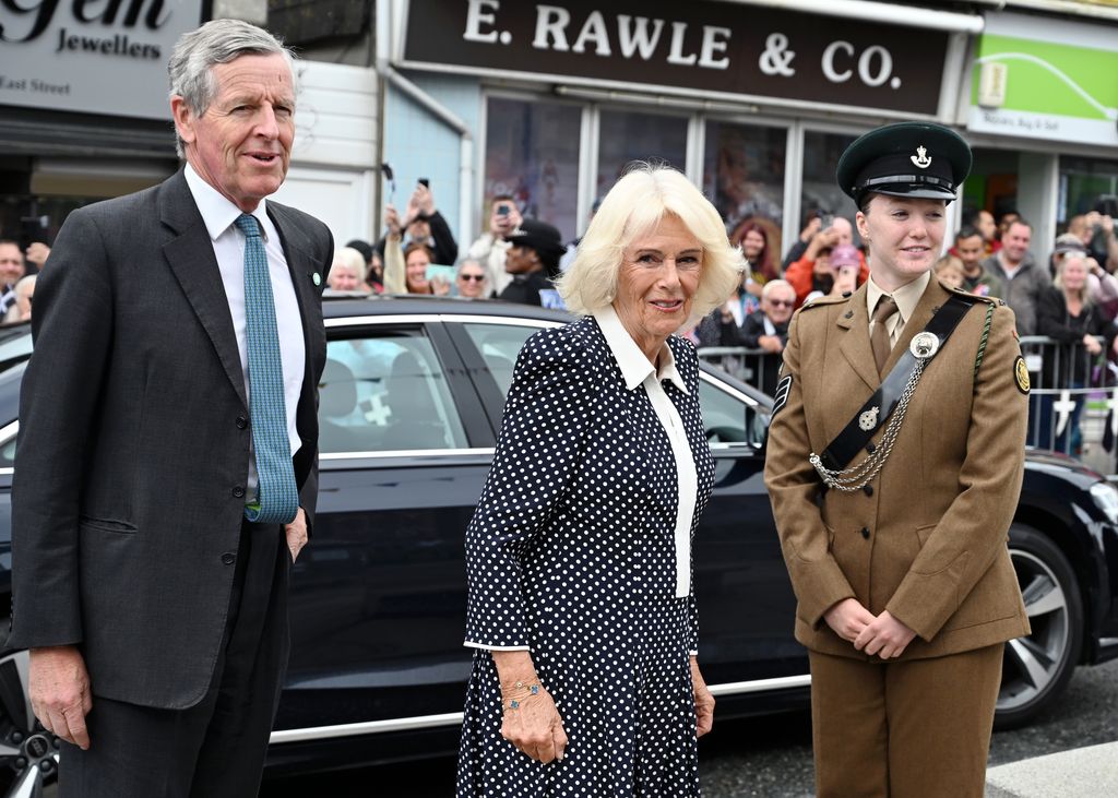 Queen Camilla standing with a man in a suit and a lady in military uniform
