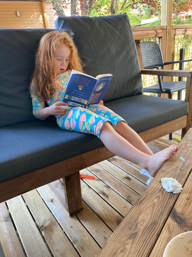 Girl with red hair reading a book on seat on decking