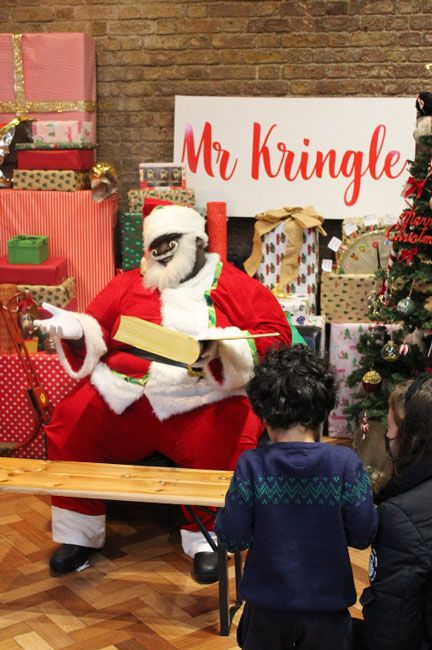 mr kringle reading to children from a large storybook surrounded by gifts