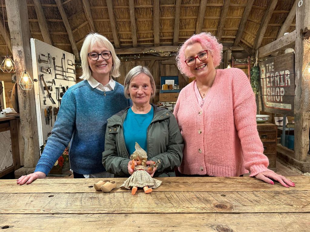 Three women posing with doll in wooden barn