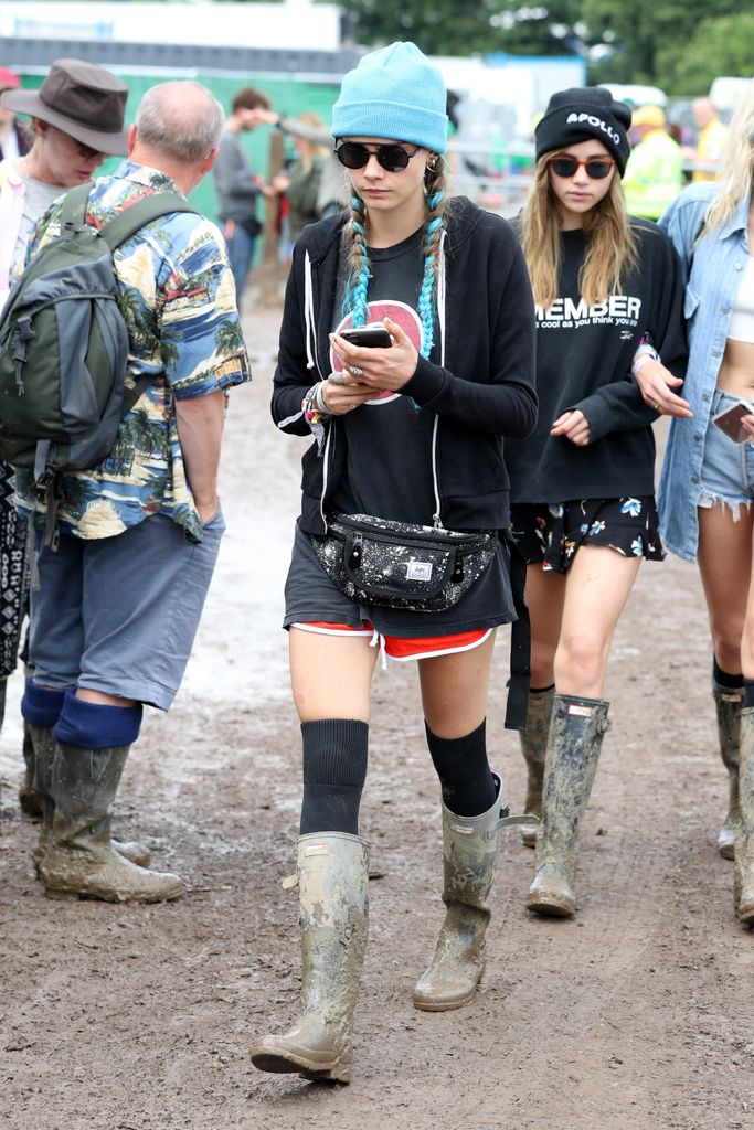 Cara Delevigne attends the Glastonbury Festival in 2016 wearing a blue beanie, red shorts, a black shirt and over-the-knee socks
