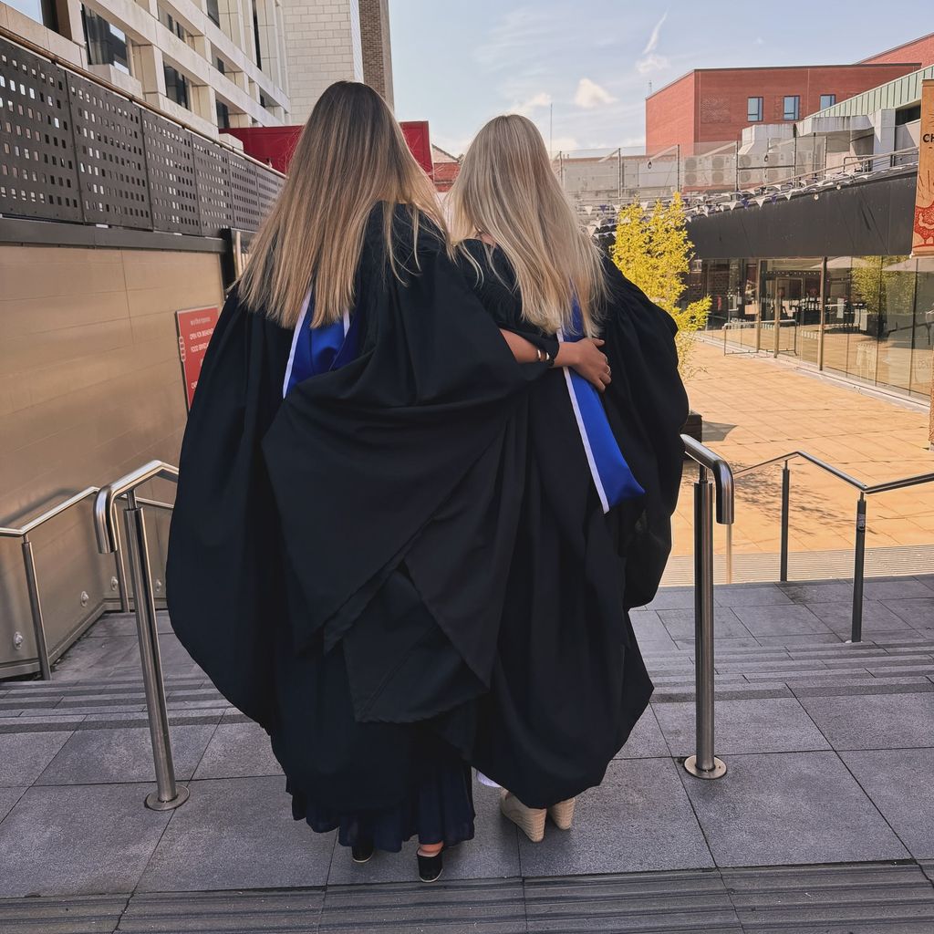 two grads posing in graduation gowns on steps