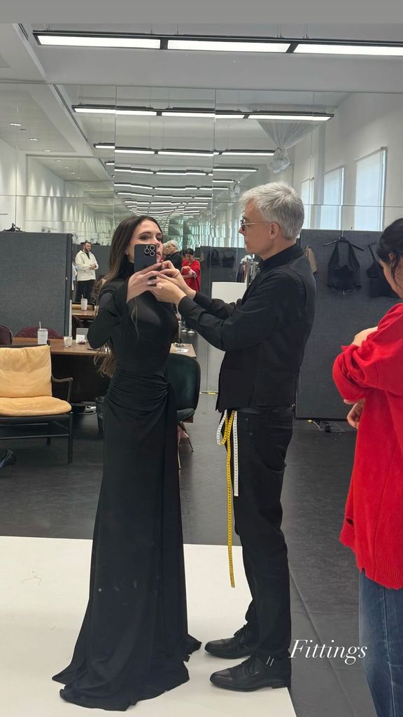 Victoria Beckham take a mirror selfie in a black gown as her tailor completes the finishing touches to the neckline