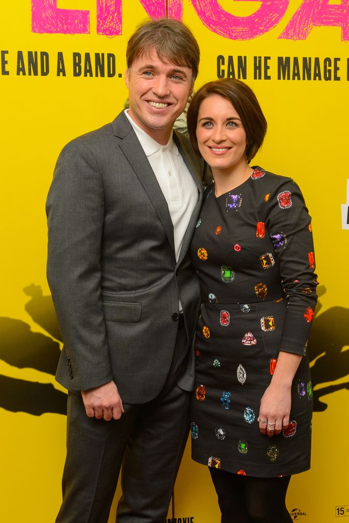 Jonny Owen in a grey suit against a yellow backdrop with Vicky McClure in a gem dress