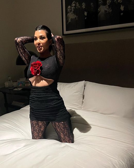 kourtney kneels on a bed in a black cut out red with a red rose