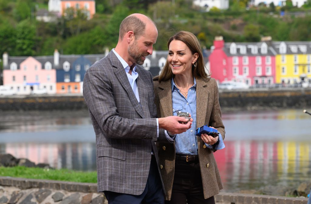 Princess Kate in a blue shirt smiling at William in front of coloured houses