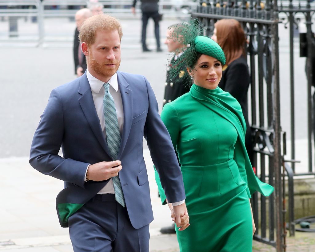 Prince Haryr in a blue suit walking with Meghan Markle in an emerald dress