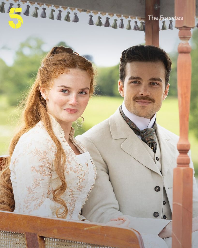 Two people in period dress sit in a carriage 