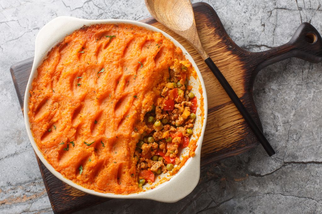 Low calorie Sweet Potato Shepherd's Pie with Turkey and Vegetables close-up in baking dish on wooden board. Horizontal top view from above