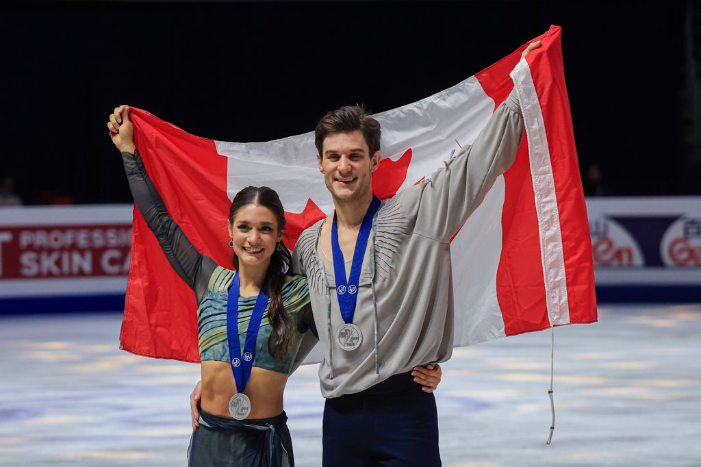 Laurence Fournier Beaudry et Nikolaj Soerensen souriant brandissant un drapeau du Canada portant des médailles d'argent sur la glace 