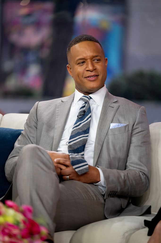 TV host in grey suit sitting on sofa in studio