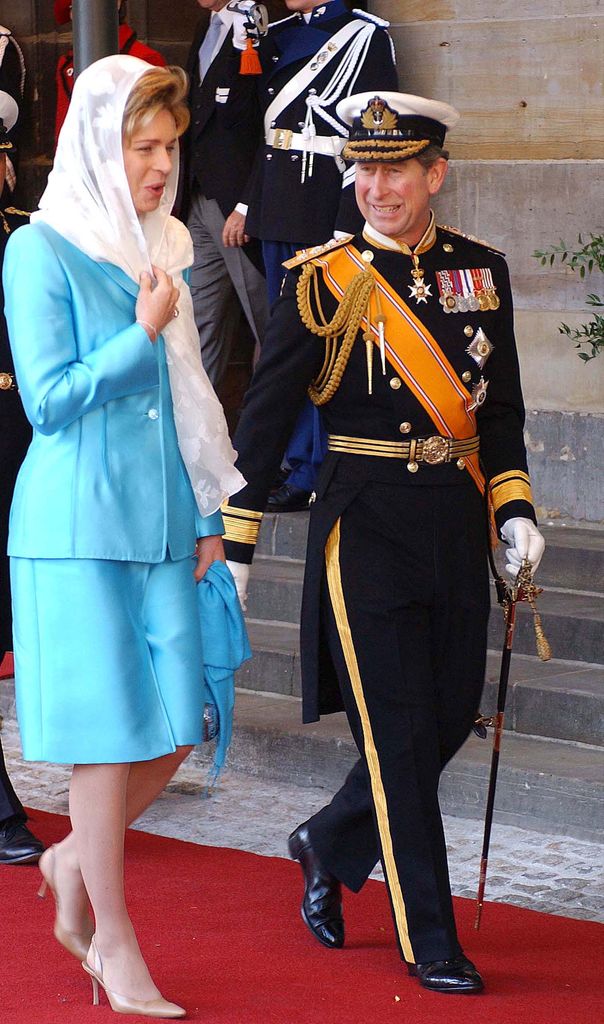 King Charles in black miliary dress uniform walking with Queen Noor of Jordan in blue skirt suit