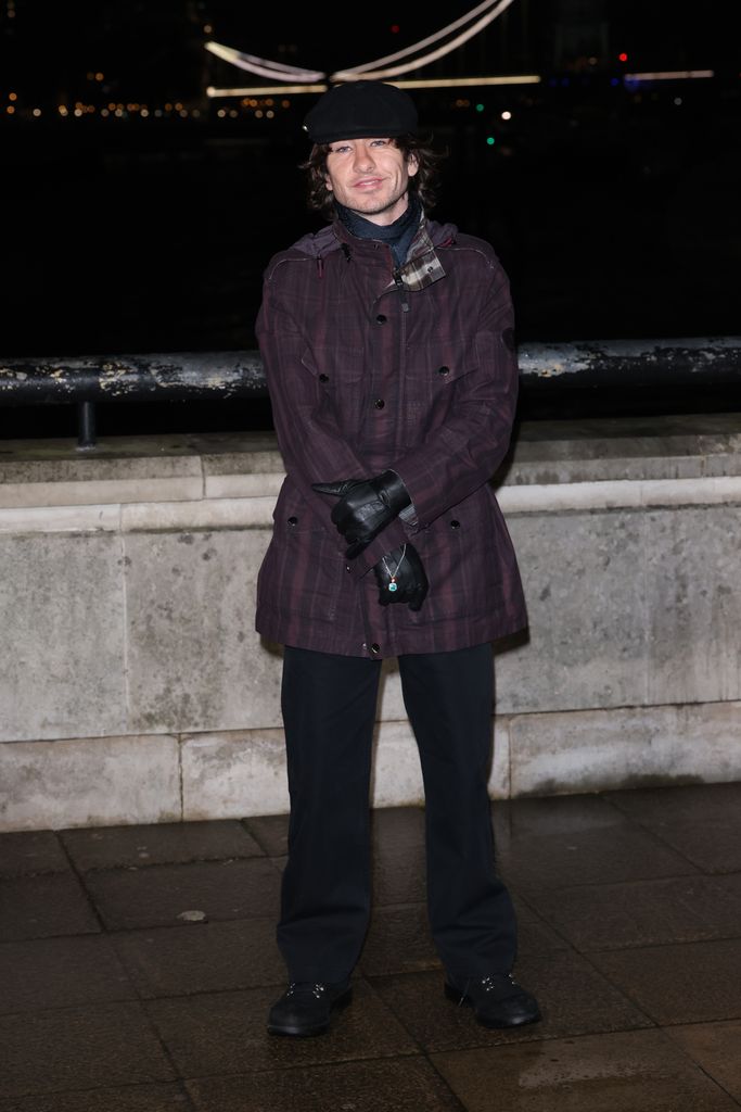 Barry Keoghan porte un trench-coat court de couleur prune, un pantalon noir et des gants