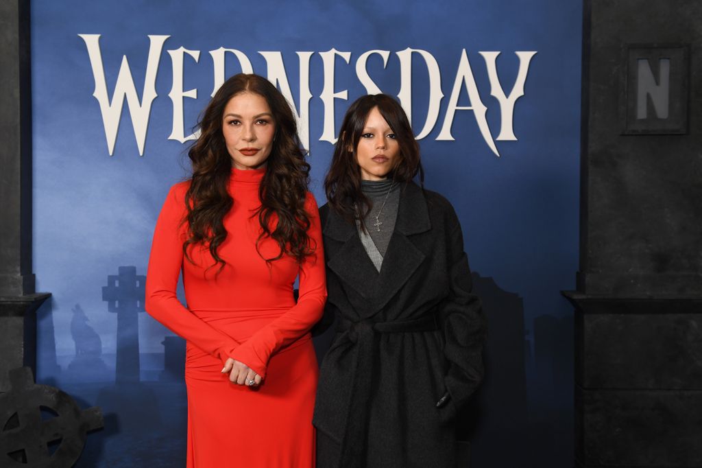 photo of catherine zeta jones in red dress next to jenna ortega in black trench coat