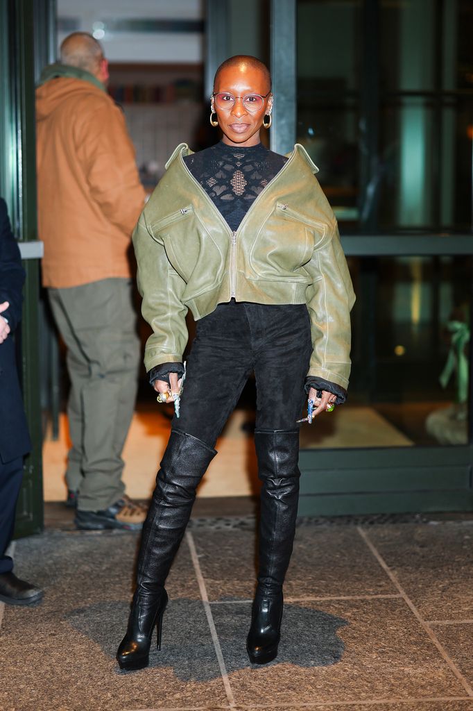 Cynthia Erivo wearing her olive green biker jacket, lacy high neck top, black trousers and black thigh high boots in New York