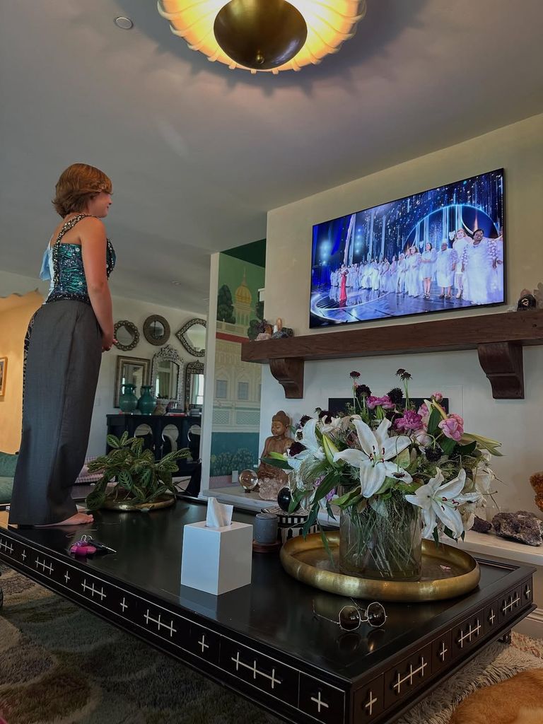 Pink's daughter, Willow, standing on black coffee table surrounded by vases facing a TV screen showing Tony award ceremony