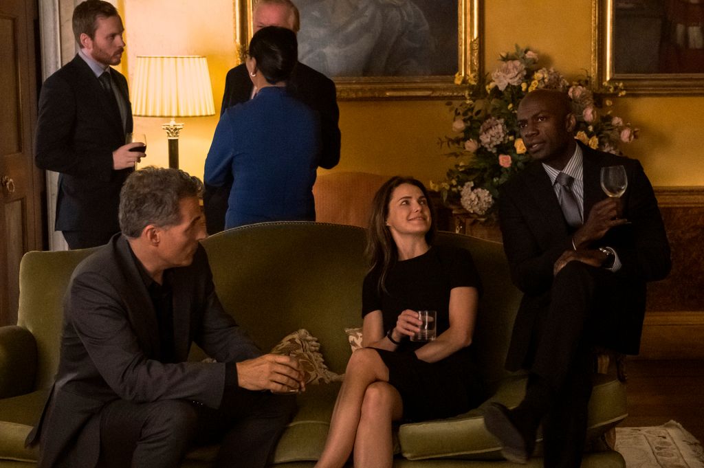The cast of The Diplomat sit on sofa and drink in episode six