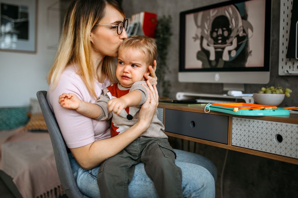 Mother holding her displeased crying baby boy son, while sitting