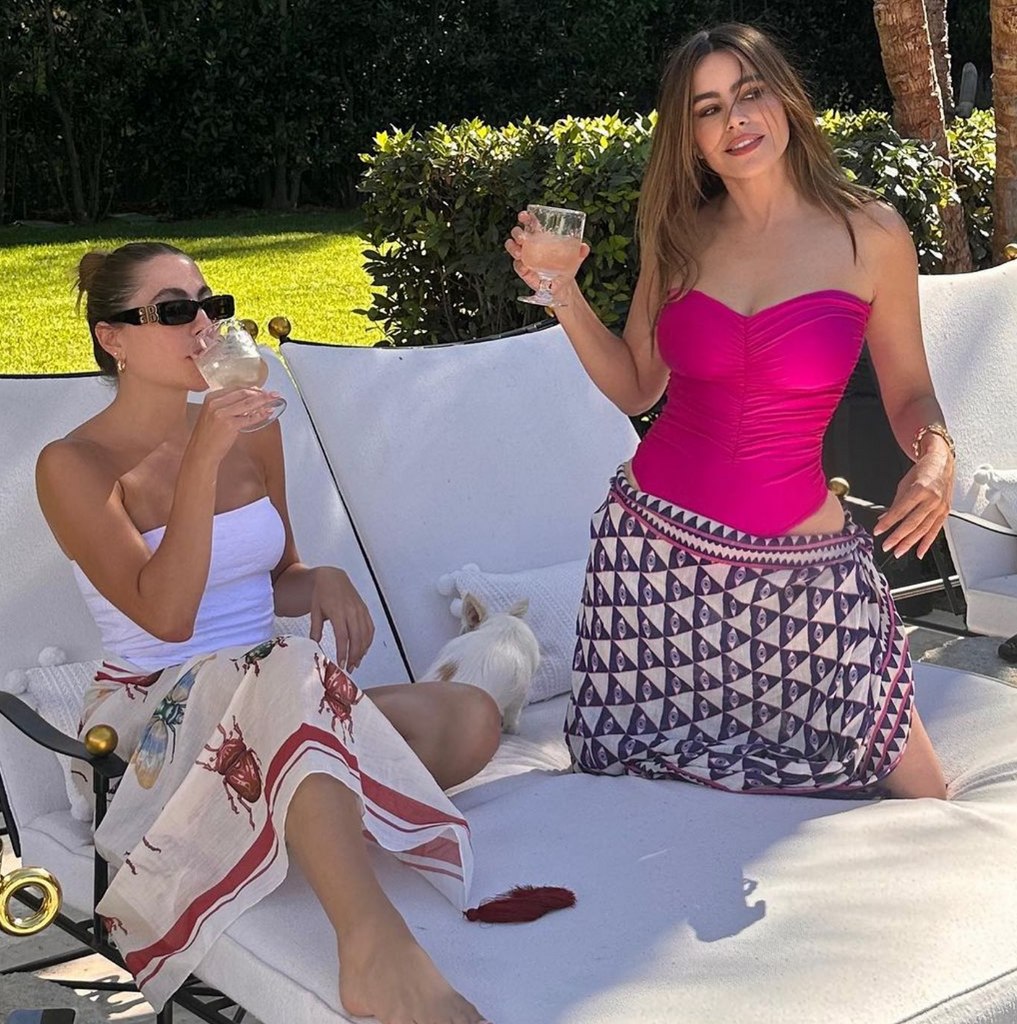 Photo posted by Sofia Vergara on Instagram August 2023 where she is wearing a strapless, hot pink swimsuit and a printed sarong, enjoying a glass of wine on a beach lounger by the pool.