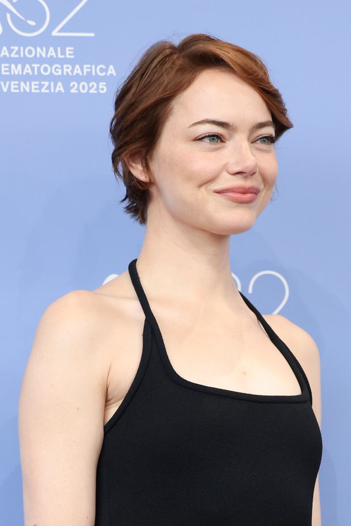 Emma Stone wears a black halterneck dress, her hair is cropped with a slight wave and her skin is radiant and glowing. 