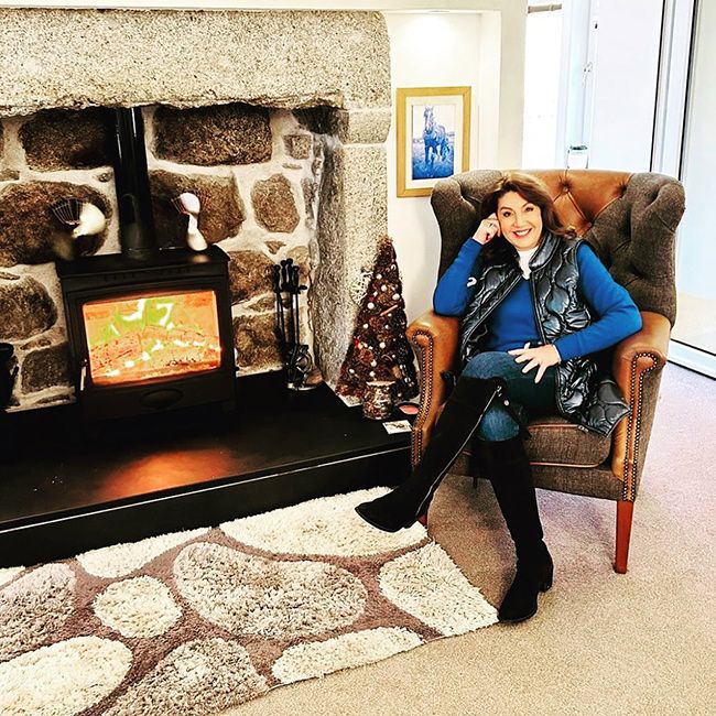 jane mcdonald posing in a chair next to a fire 