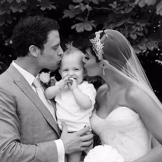 a black and white photo of a bride and groom holding a giggling baby as they both lead in to kiss the child on either side of its head