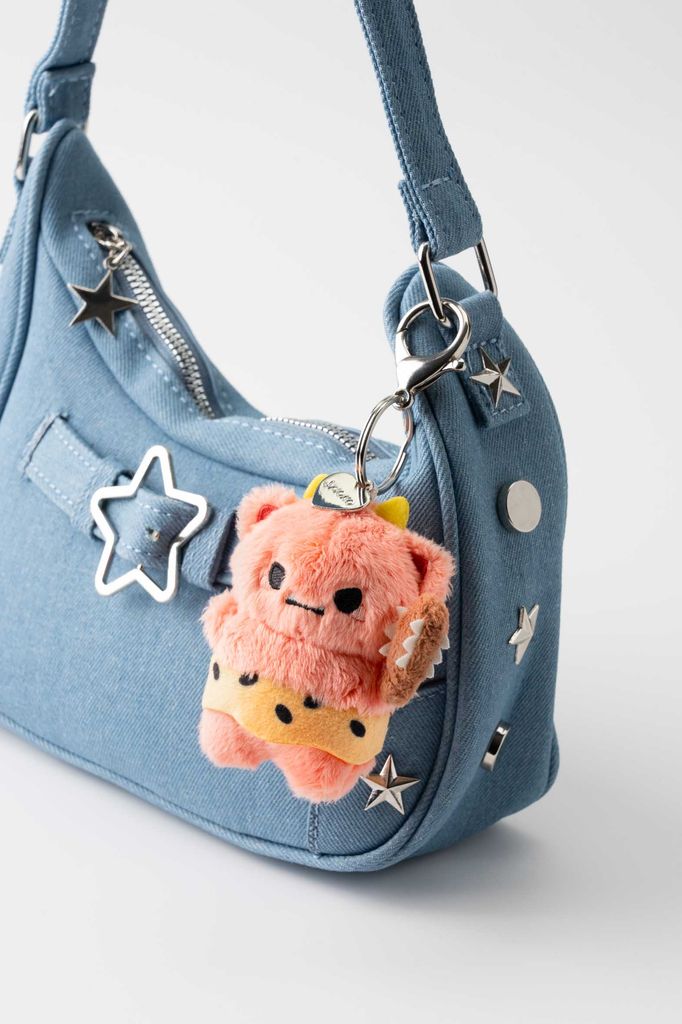 A small pink fluffy bag charm on a denim handbag