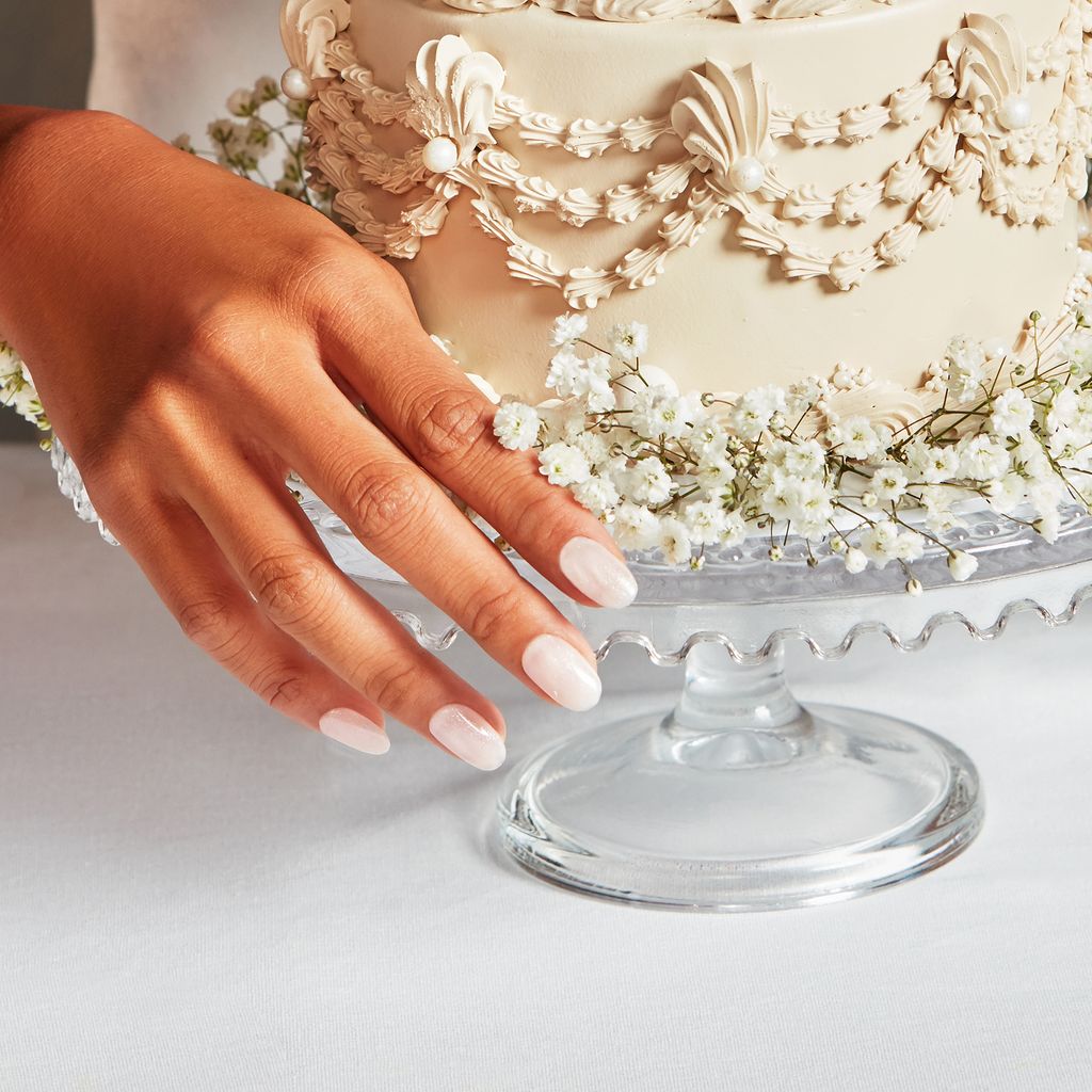 Woman with pale pink nails next to a wedding cake