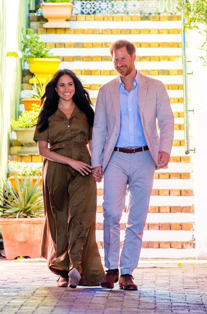 Meghan Markle sorrindo em um vestido verde com seu marido, o príncipe Harry