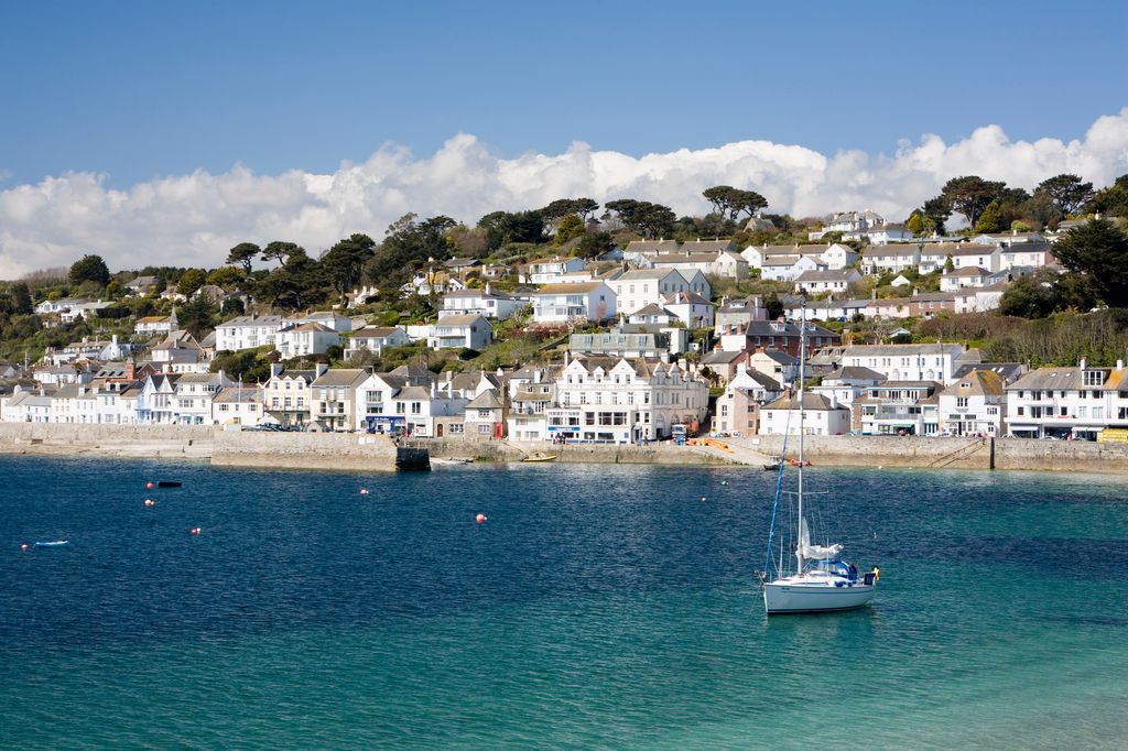 A yacht floating on the clear blue water in the small seaside harbour and coastal town of St Mawes.