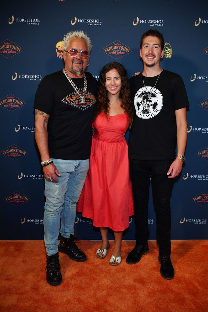 Guy Fieri, Tara Bernstein and Hunter Fieri pose on the orange carpet at the grand opening celebration of Guy Fieri's Flavortown Sports Kitchen at Horseshoe Las Vegas on July 07, 2023 in Las Vegas, Nevada