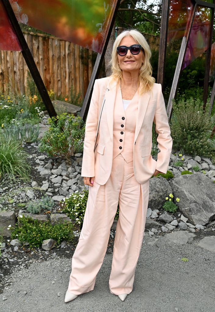 Gaby Roslin wears a pale pink tailored suit with wide-leg trousers and black buttons poses with sunglasses at Chelsea Flower Show 2025.