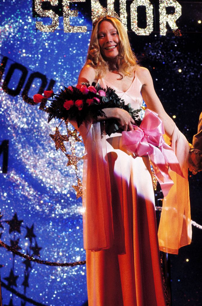 Sissy Spacek wearing pink dress holding flowers in film Carrie
