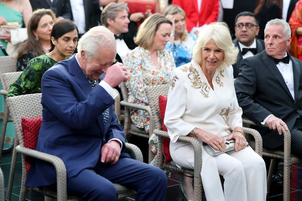 King Charles and Queen Camilla laughing while sitting in chairs