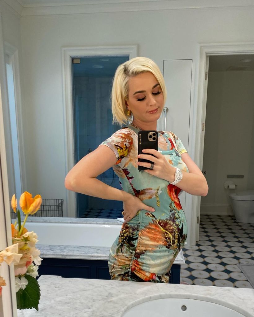 Katy Perry in a tight floral dress taking a mirror selfie in the bathroom 