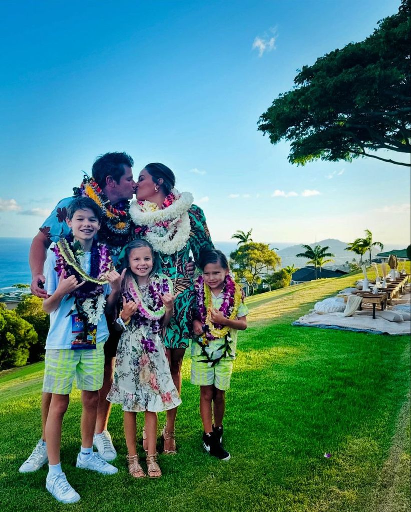 Vanessa Lachey and Nick Lachey lean in for a kiss while posing wearing leis with their three children, shared on Instagram